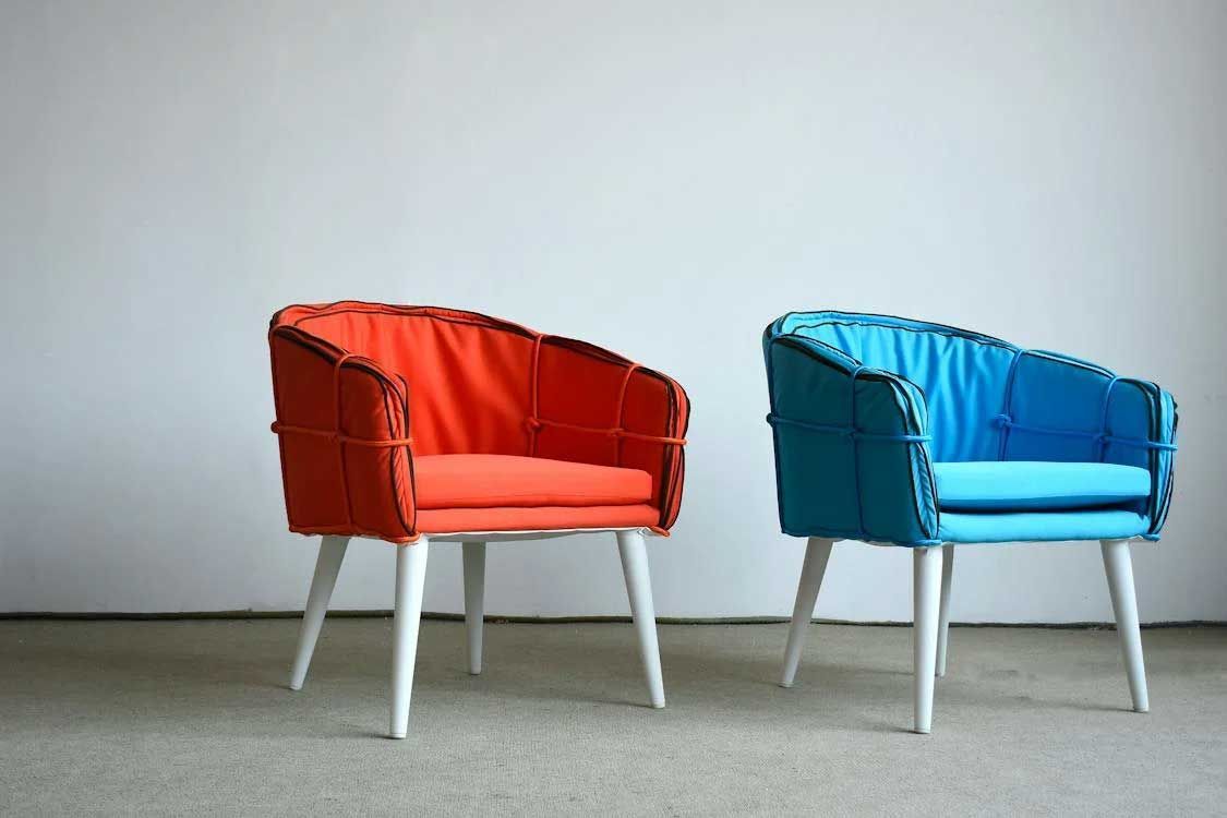 Two modern chairs, one red and one blue, on a gray floor against a white wall.
