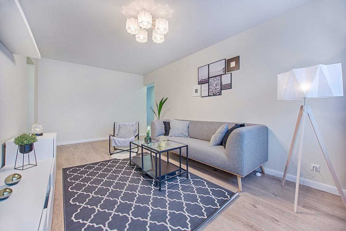 Bright living room with gray sofa, patterned rug, glass coffee table, and floor lamp