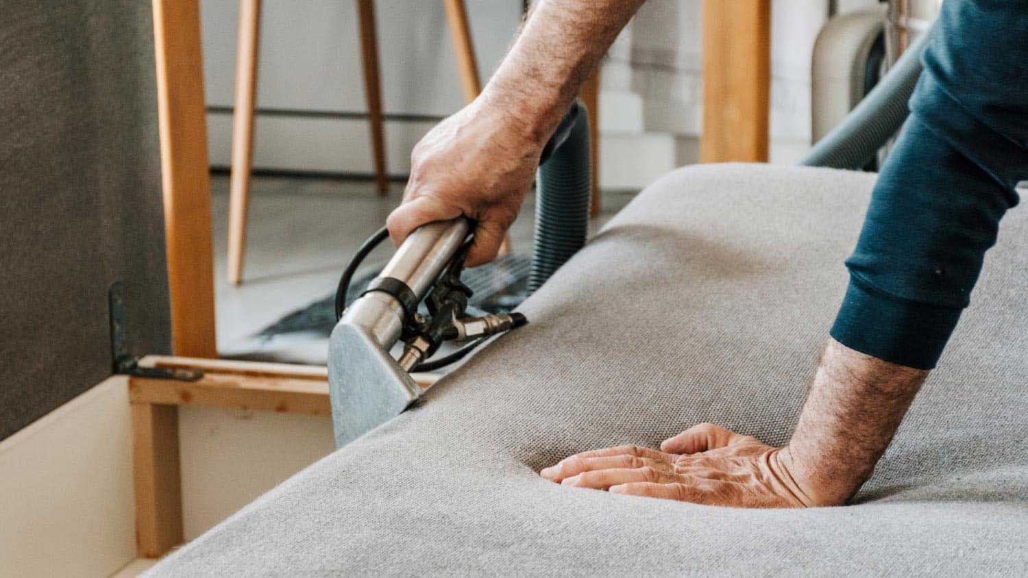 Upholstery cleaning with a handheld vacuum on a light gray sofa fabric