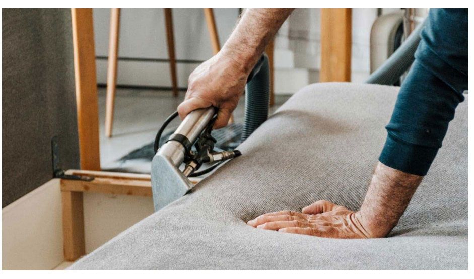 Hands using a staple gun to upholster a gray sofa cushion