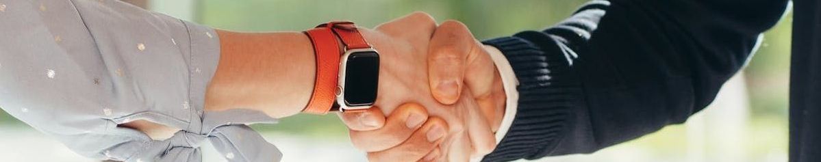Two people shaking hands, one wearing a smartwatch with a red band.