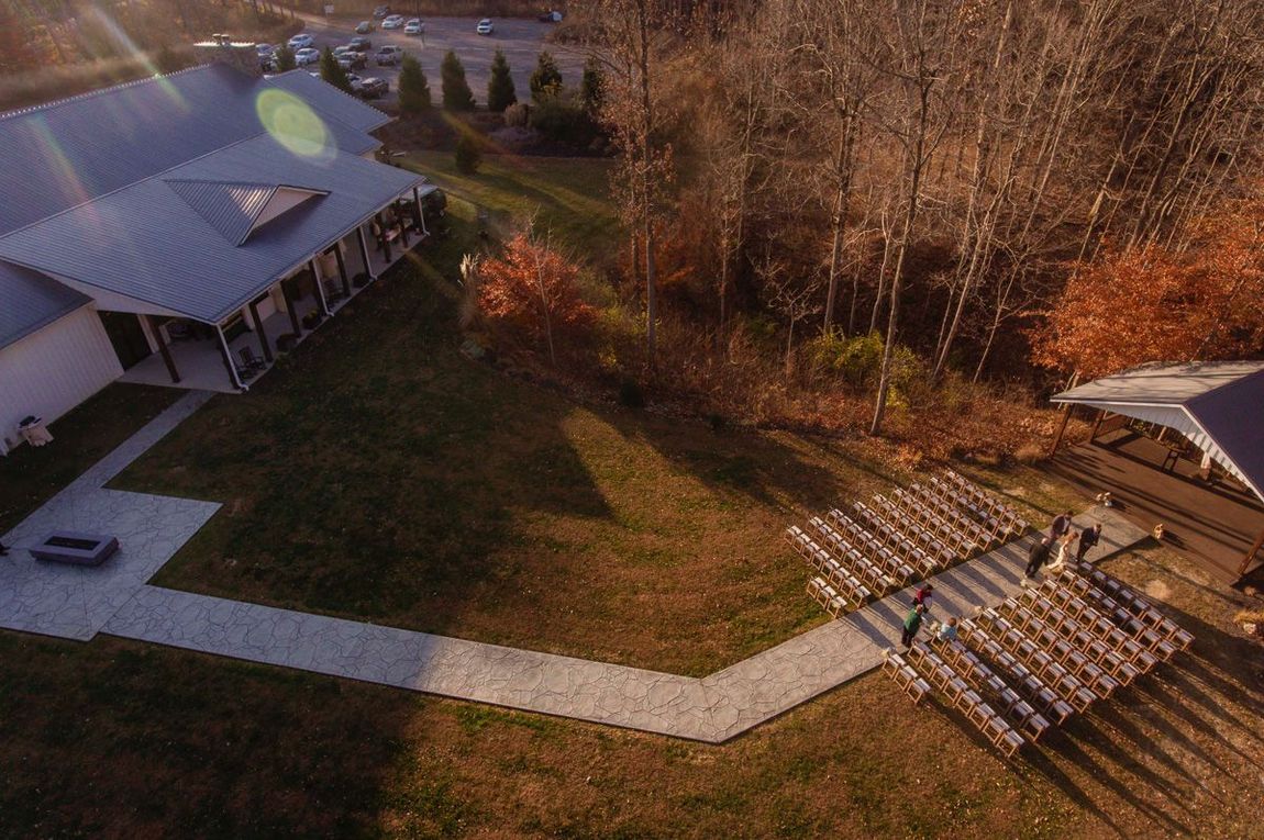 Aerial view of a building, walkway, and empty outdoor seating area beside trees in autumn sunlight