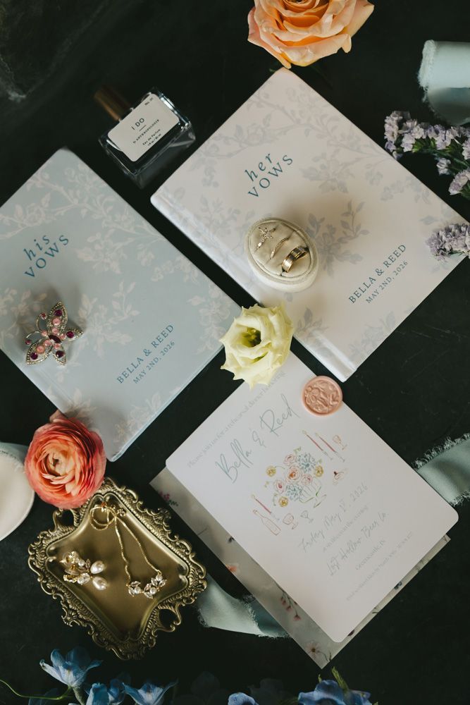 Four pastel invitation cards with dried flowers and gold accents on a dark surface.