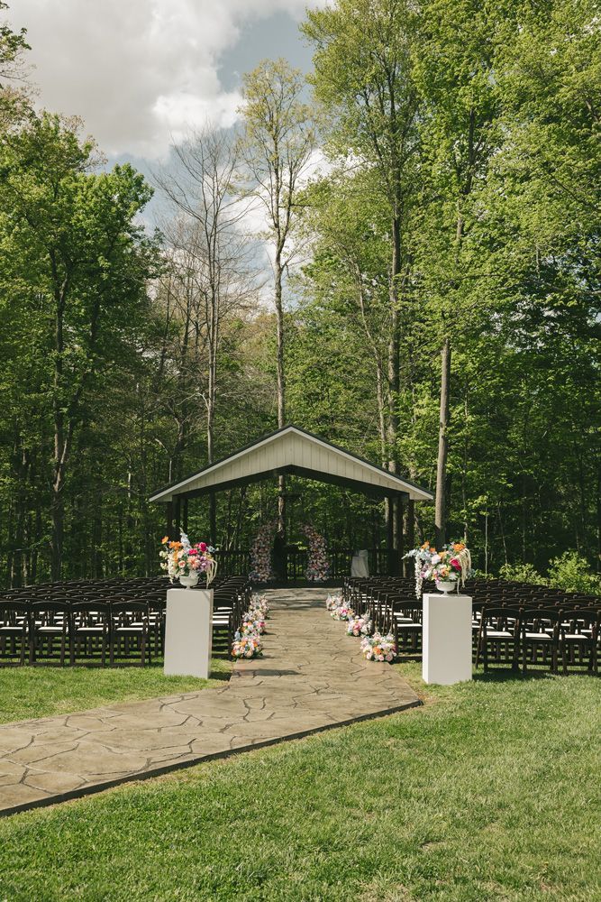 Outdoor wedding altar with white flower stands and chairs under a canopy in a wooded clearing
