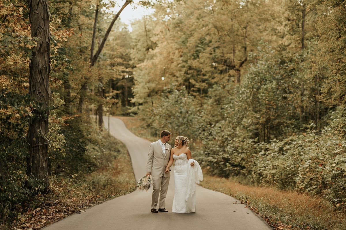Bride and groom walking hand in hand on a winding tree-lined road outdoors