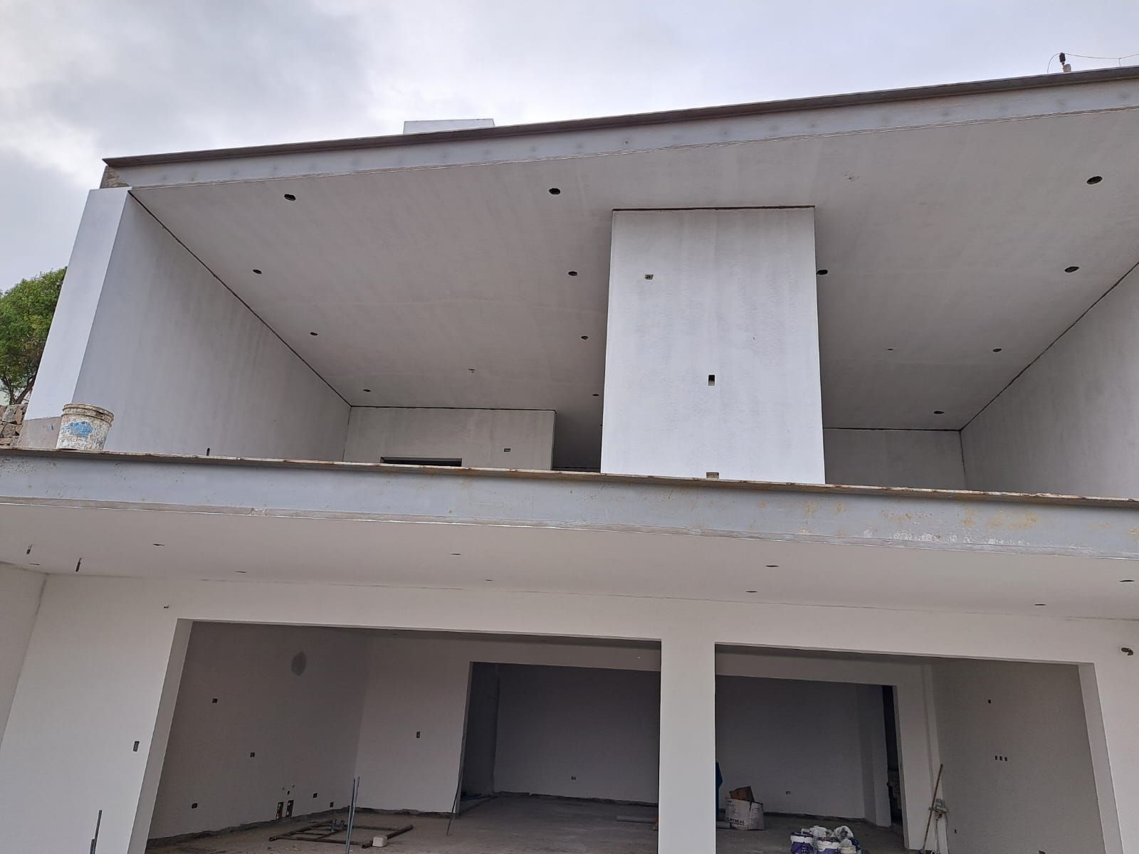 Cinco trabajadores con chalecos amarillos miden y pintan una pared interior blanca en obras.
