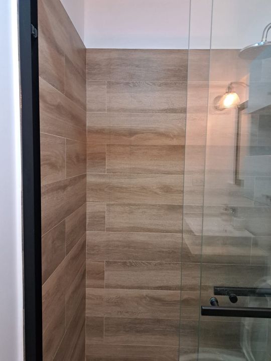 Persona aplicando pintura blanca a una pared con un rodillo y una brocha en una habitación luminosa.