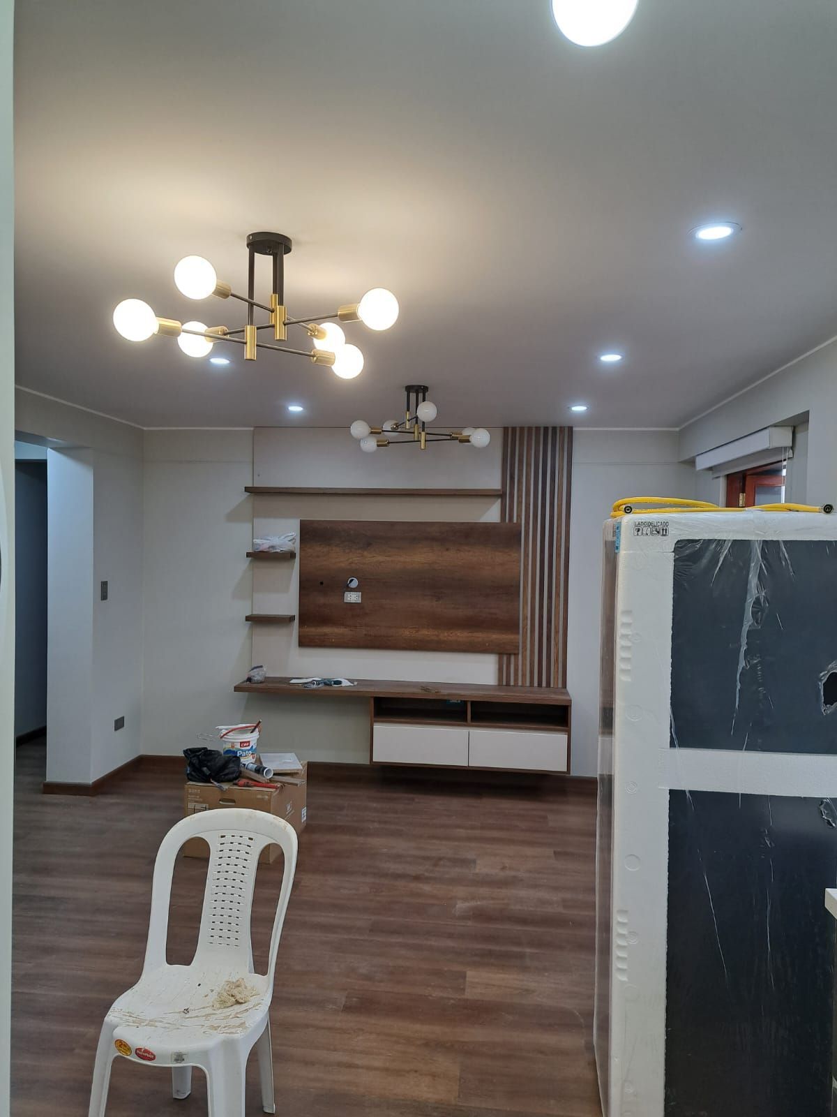 Habitación vacía con suelos de madera clara y una pared blanca parcialmente pintada con una zona de reparación de paneles de yeso irregular.