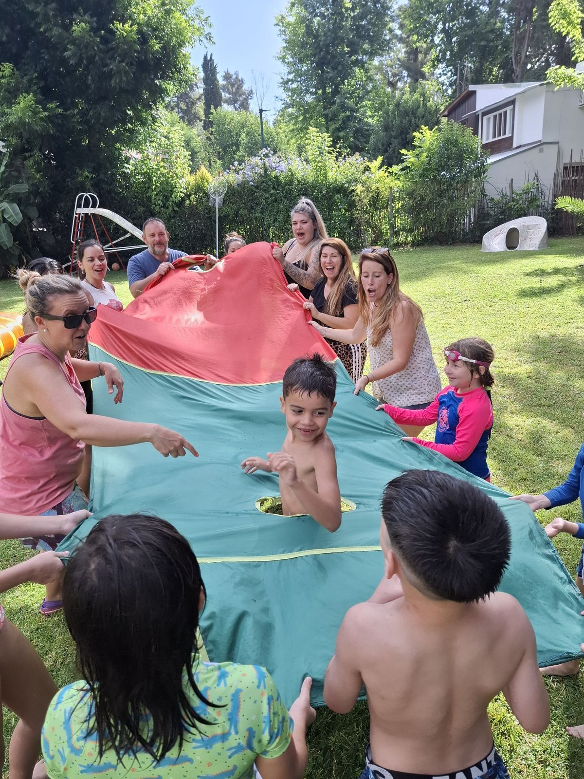 Niños y adultos jugando al aire libre con un paracaídas rojo y verde.