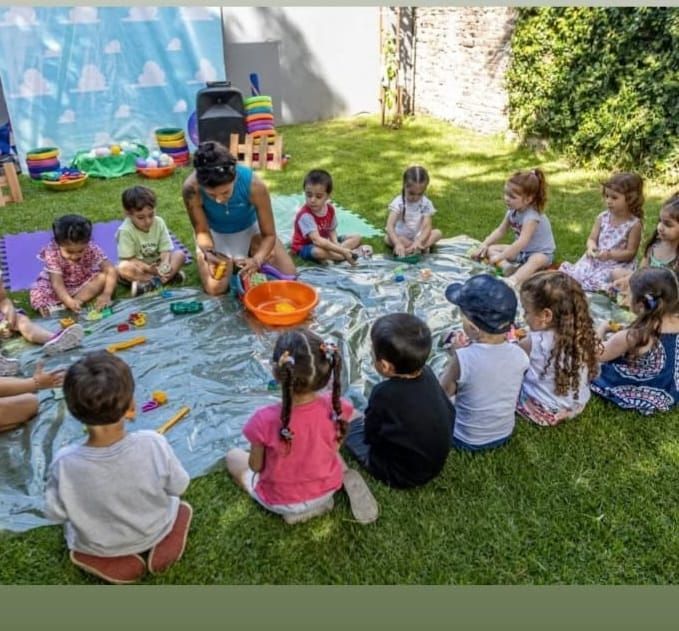Unos niños y una mujer estaban reunidos al aire libre sobre el césped, jugando con juguetes.