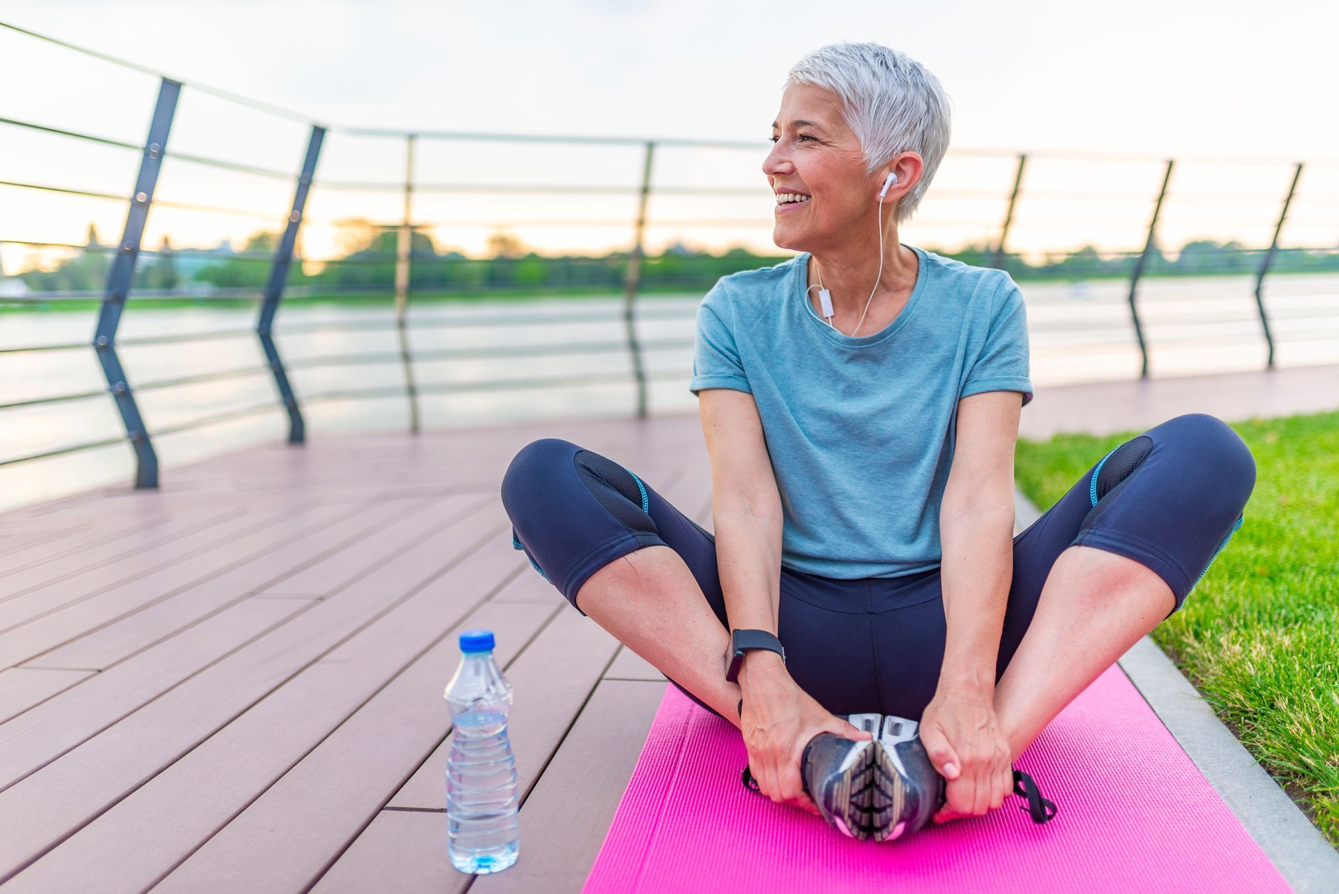 Person Stretching on a Pink Yoga Mat Outdoors Beside a Water Bottle at Sunset — Fraser Shores Hair Design In Urraween, QLD