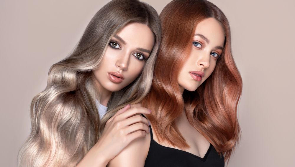 Two Women With Long Wavy Hair Posing Against a Soft Beige Background — Fraser Shores Hair Design In Urraween, QLD