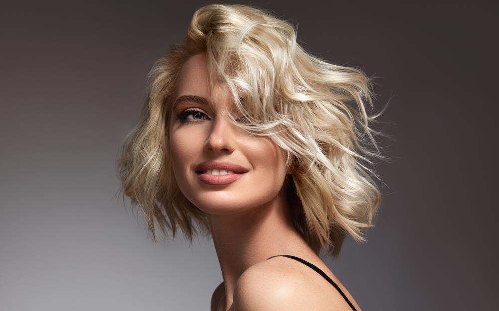 Portrait of A Smiling Blonde Person with Tousled Hair on A Gray Background — Fraser Shores Hair Design In Urraween, QLD