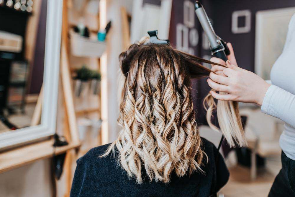 Hair Stylist Curling Shoulder-Length Blonde Hair — Fraser Shores Hair Design In Urraween, QLD
