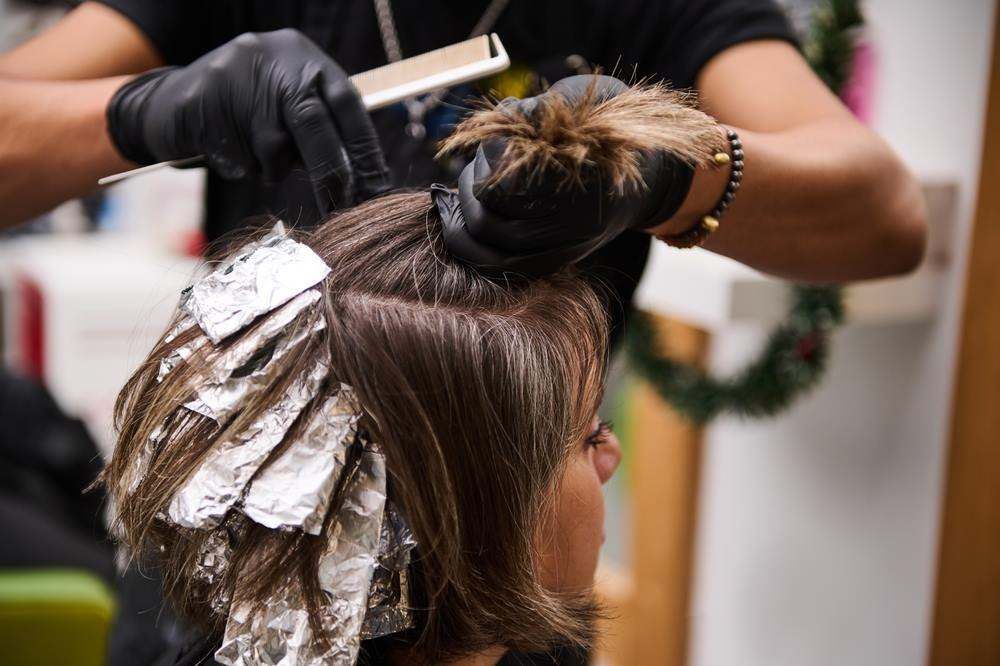 Hair Stylist Applying Foils to A Client’s Brown Hair in A Salon — Fraser Shores Hair Design In Urraween, QLD