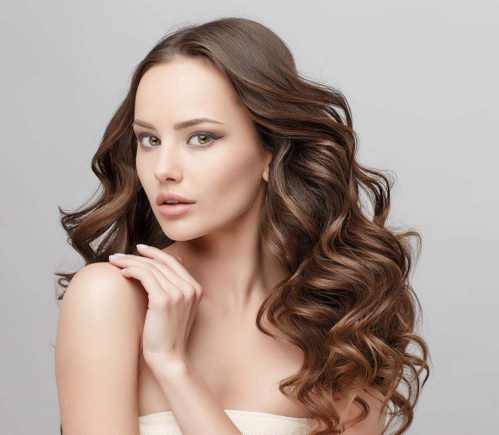 Portrait of A Woman with Long Wavy Brown Hair Against a Light Gray Background — Fraser Shores Hair Design In Urraween, QLD