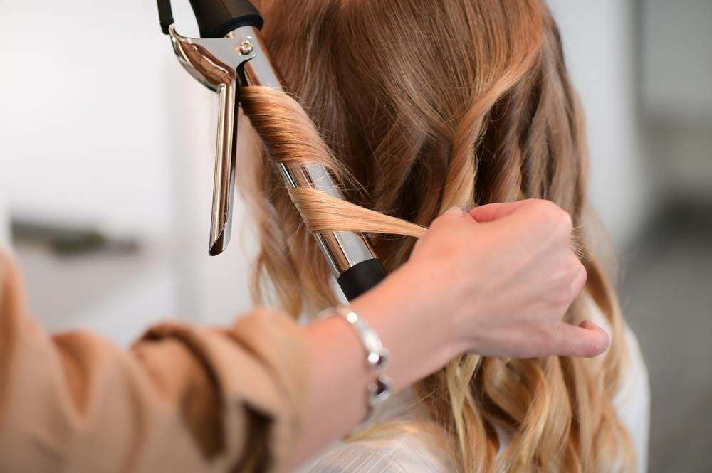 Stylist Curling Blonde Hair with A Curling Iron in A Salon — Fraser Shores Hair Design In Urraween, QLD