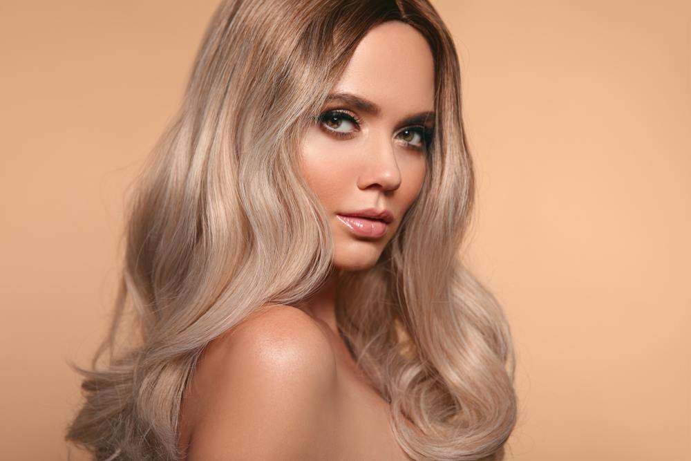 Portrait of A Person with Long Wavy Blonde Hair Against a Warm Beige Background — Fraser Shores Hair Design In Urraween, QLD