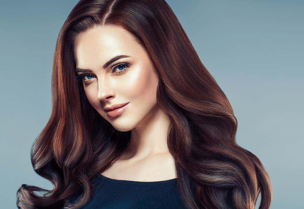 Portrait of A Woman with Long Wavy Brown Hair Against a Soft Blue Background — Fraser Shores Hair Design In Urraween, QLD