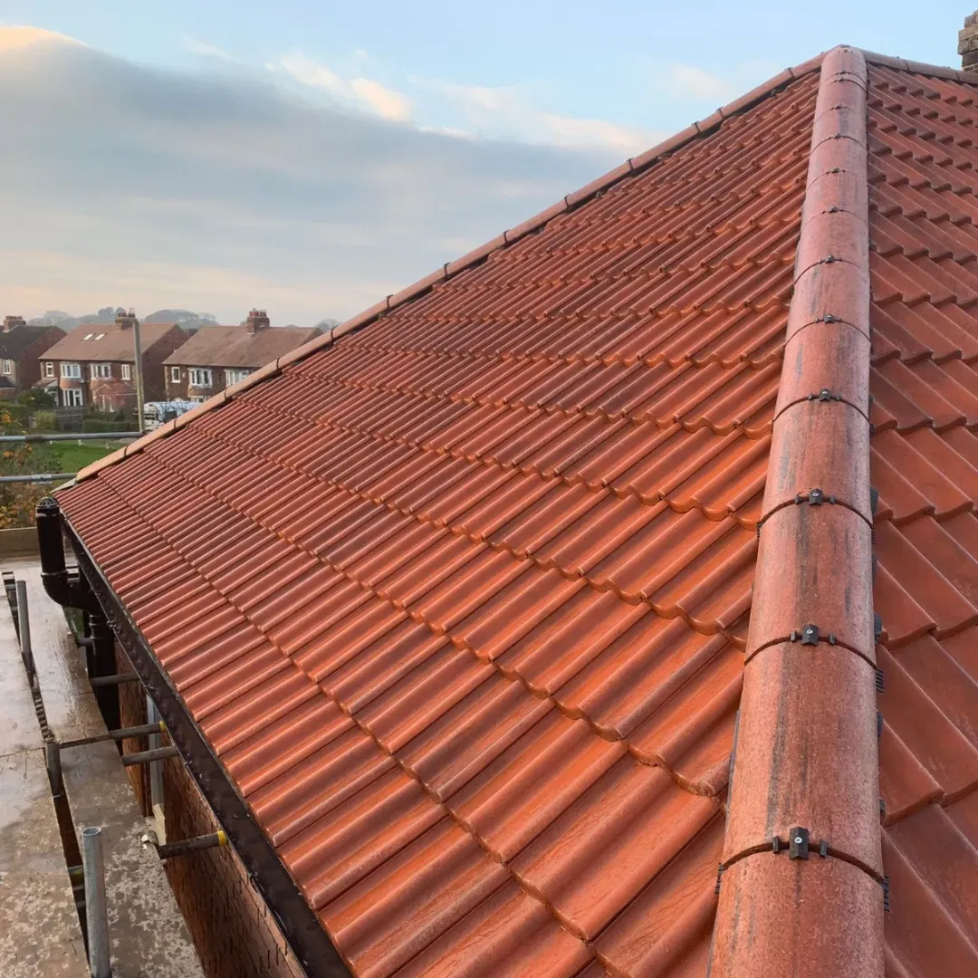 Red tiled roof on a house, with a cloudy sky and suburban houses in the background.