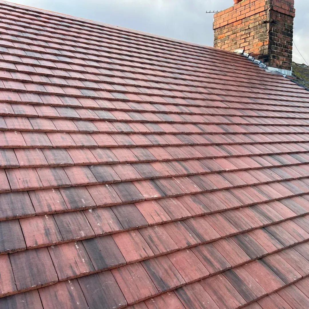 Red tiled roof with brick chimney against a cloudy sky.