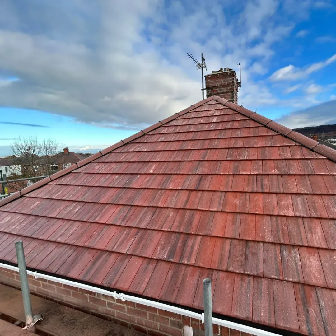 Red tiled roof with chimney against a blue sky.