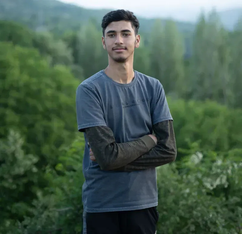 Person standing with arms crossed in a blue shirt in a green mountain landscape