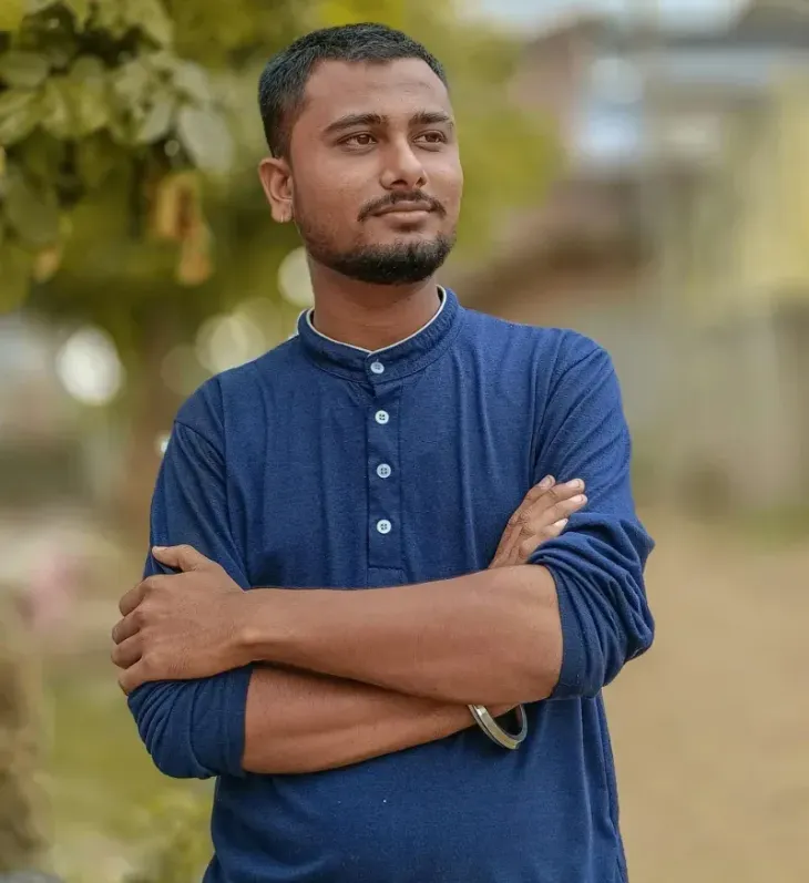 Man in a blue shirt standing outdoors with arms crossed, looking off to the side.