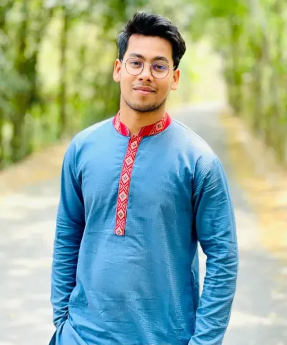 Person in a blue embroidered kurta standing on a tree-lined path, with a slight smile.