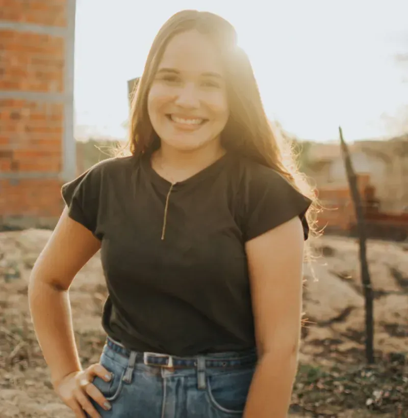 Smiling person in a black shirt and jeans standing outdoors in warm sunlight.