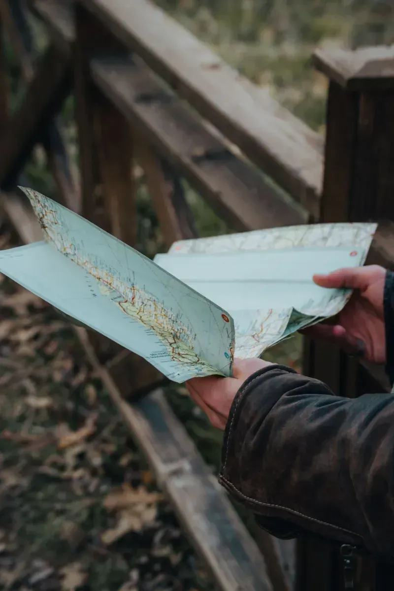 Hands hold an open notebook with pale blue pages, outdoors by a wooden fence.