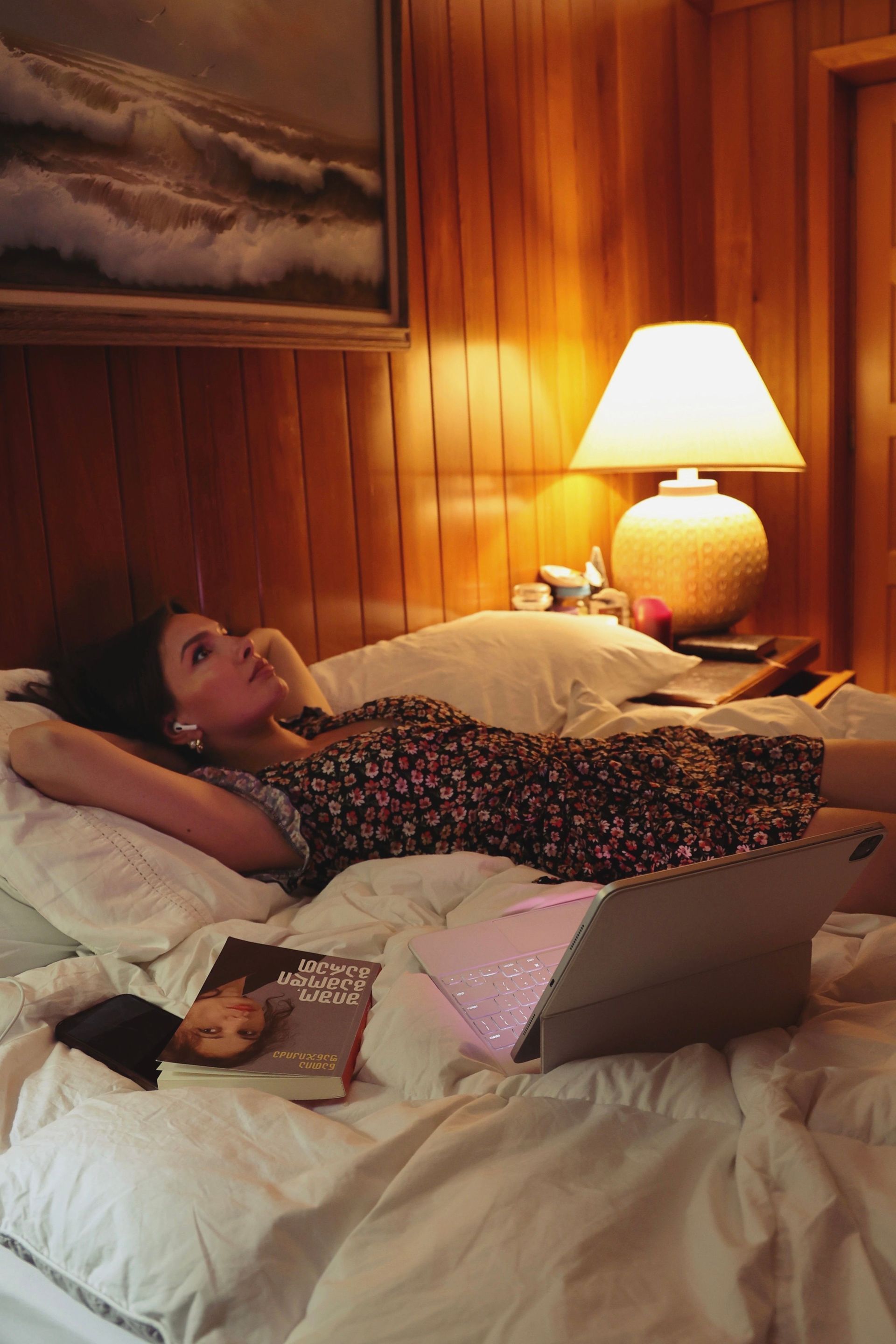 Person laying on a bed overthinking decisions with a laptop in a warm, wood-paneled room beside a lit lamp