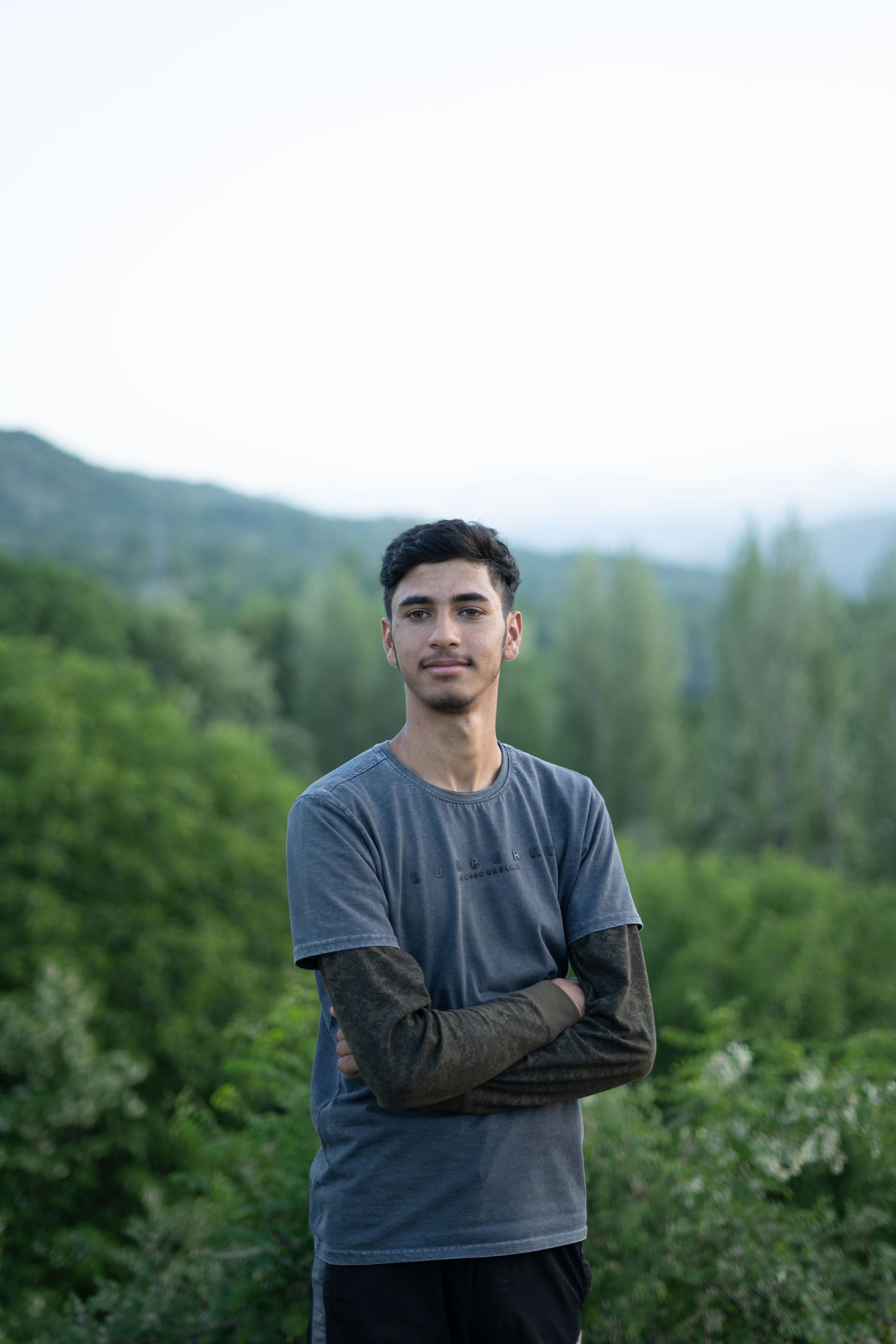 Person standing with arms crossed in a blue shirt in a green mountain landscape