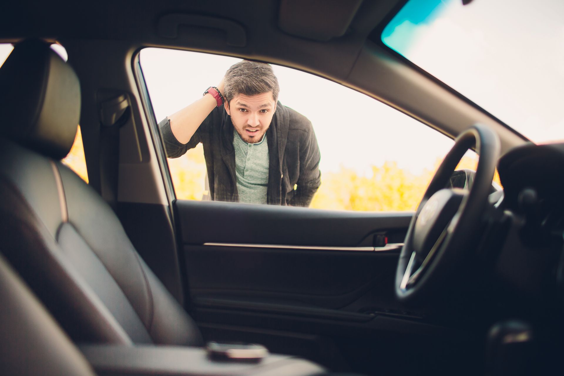A man stands outside the car, looking in with a worried, locked-out expression. A man stands outside the car, looking in with a worried, locked-out expression.