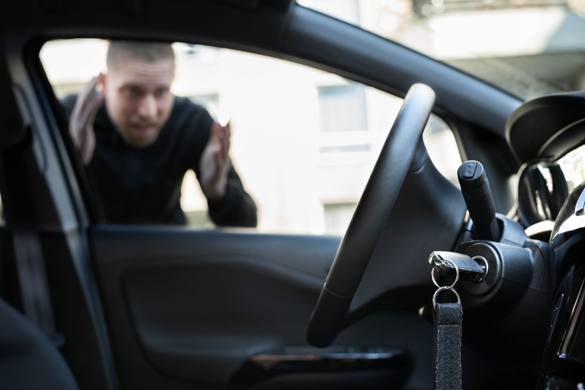 View from inside a car with keys in ignition, person outside gesturing toward driver’s seat. View from inside a car with keys in ignition, person outside gesturing toward driver’s seat.
