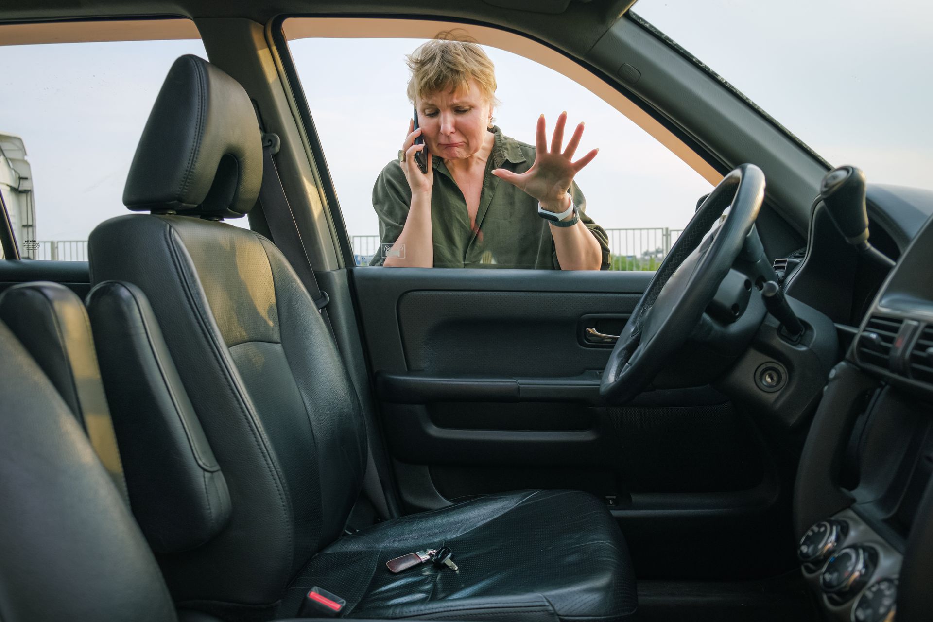 Distressed woman on phone after seeing locked keys in car seat through the window.