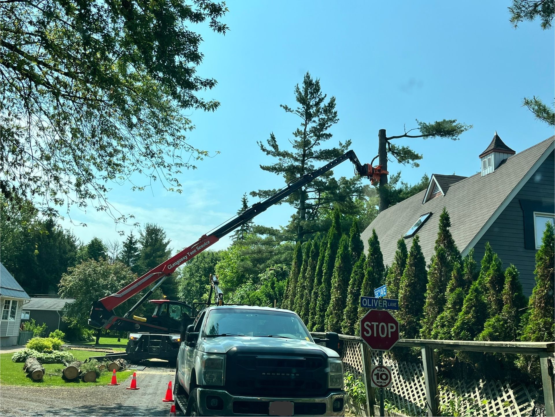 Truck with lift trimming a tree near a house. Roadside with stop sign and safety cones.
