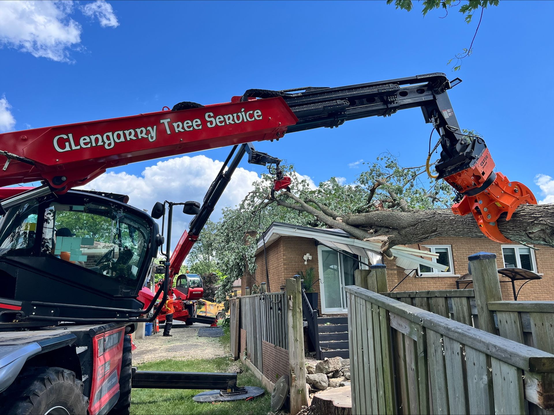 Red tree service machine with grappling arm removing tree branches from a house.