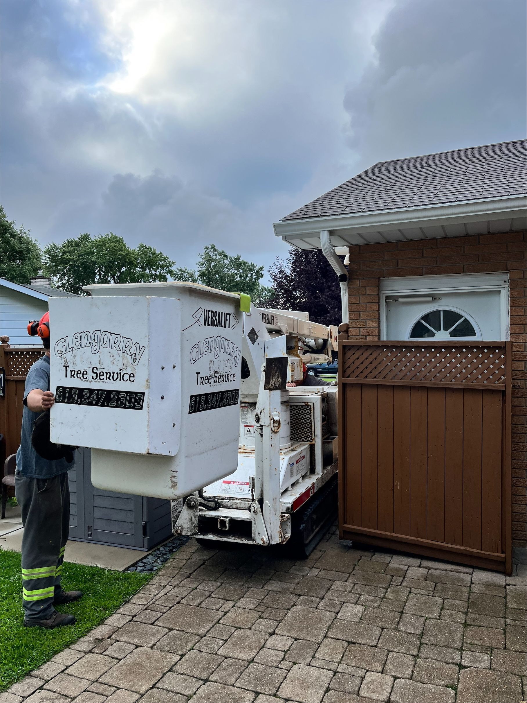 White bucket truck near a house, a person in safety gear is nearby.