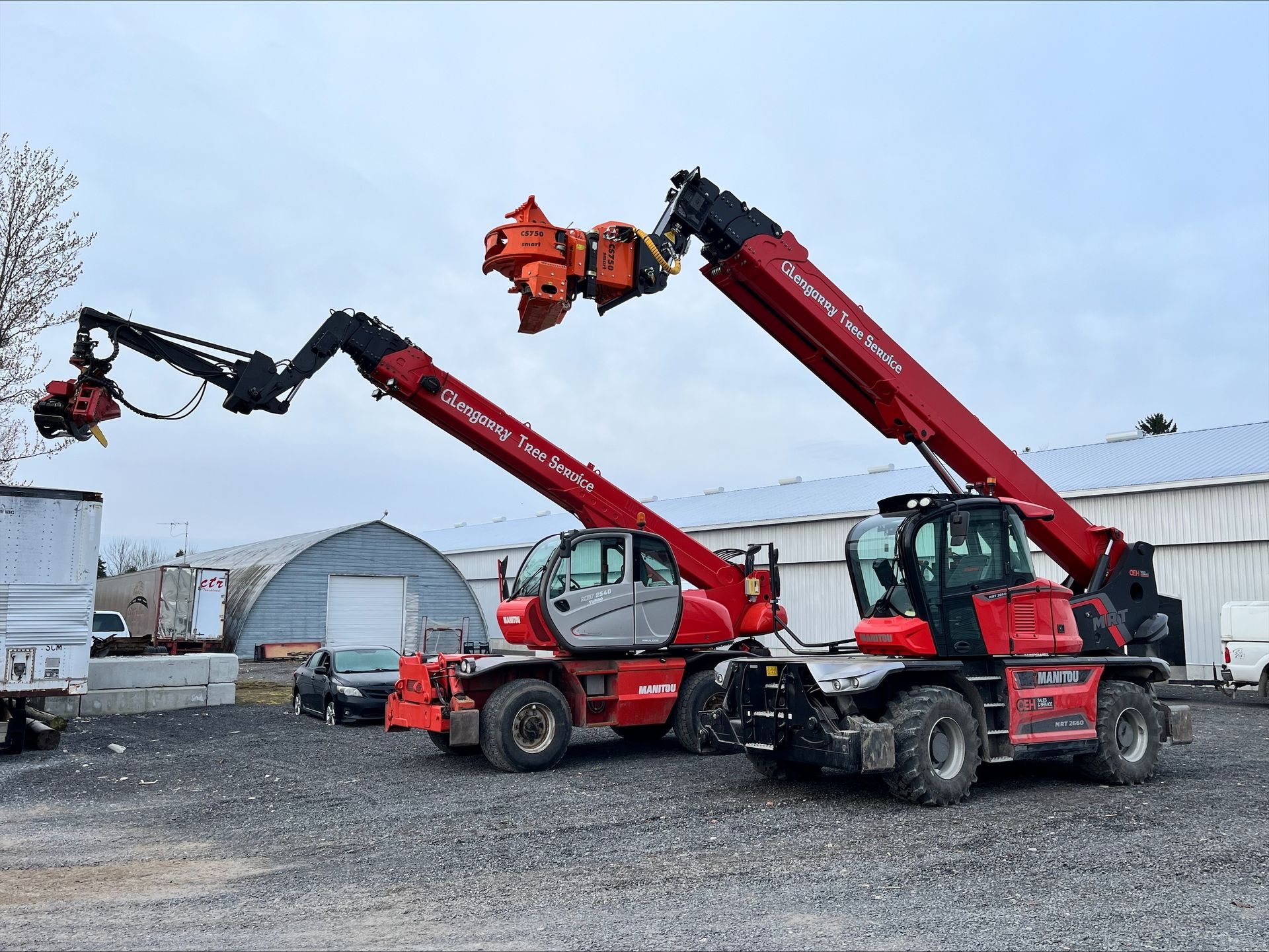 Two red telescopic handlers with attachments parked on gravel.