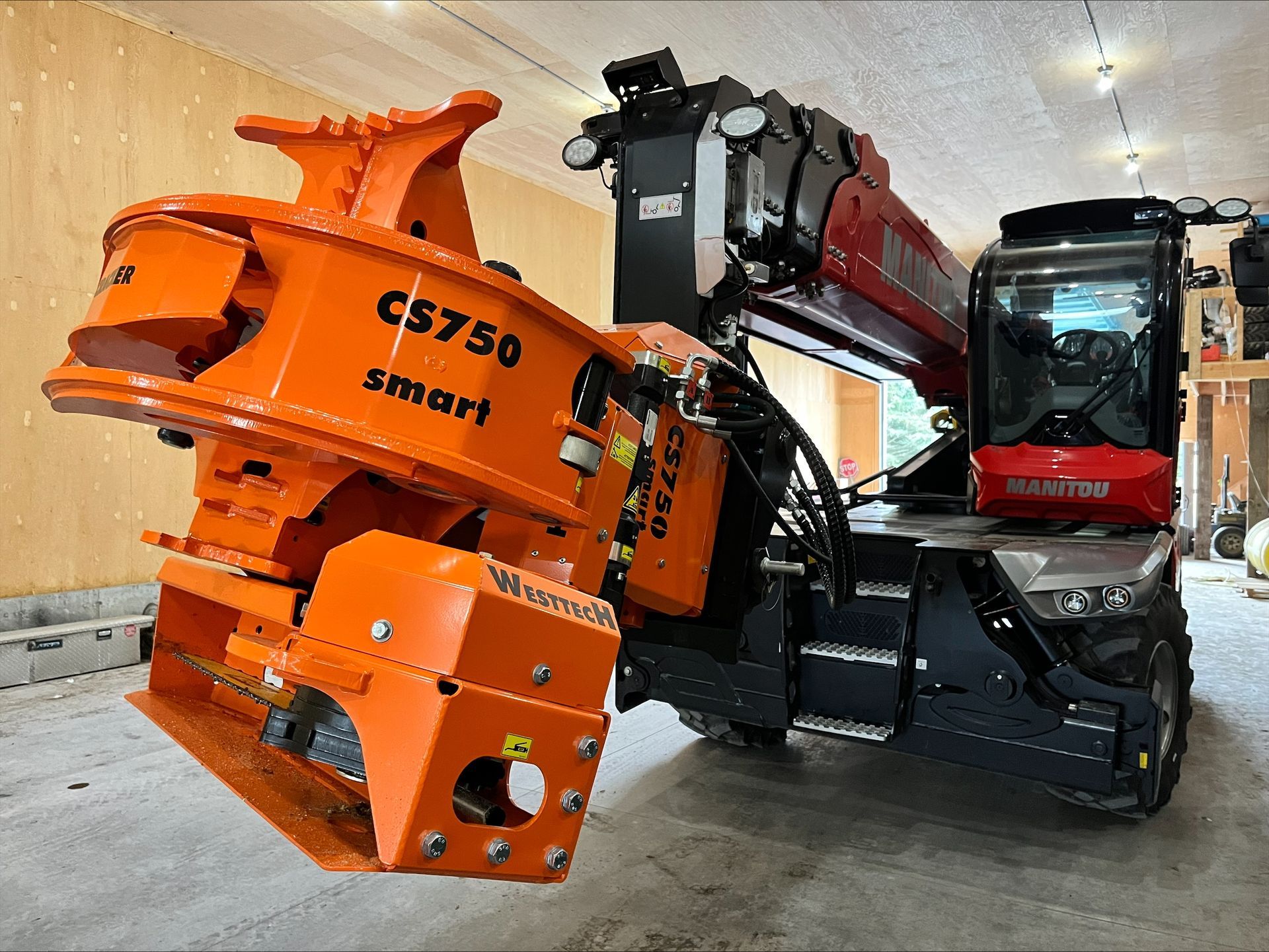 Orange CS750 smart grapple attached to a red Manitou telehandler in a construction setting.