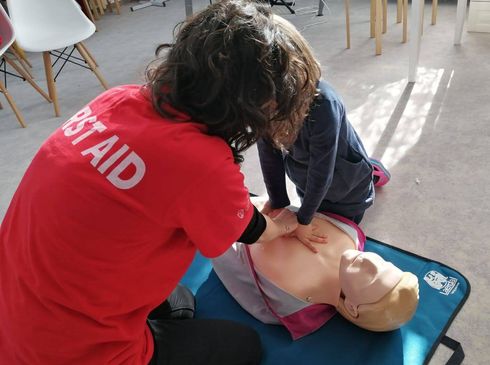 A woman in a red first aid shirt is giving a child a heart massage