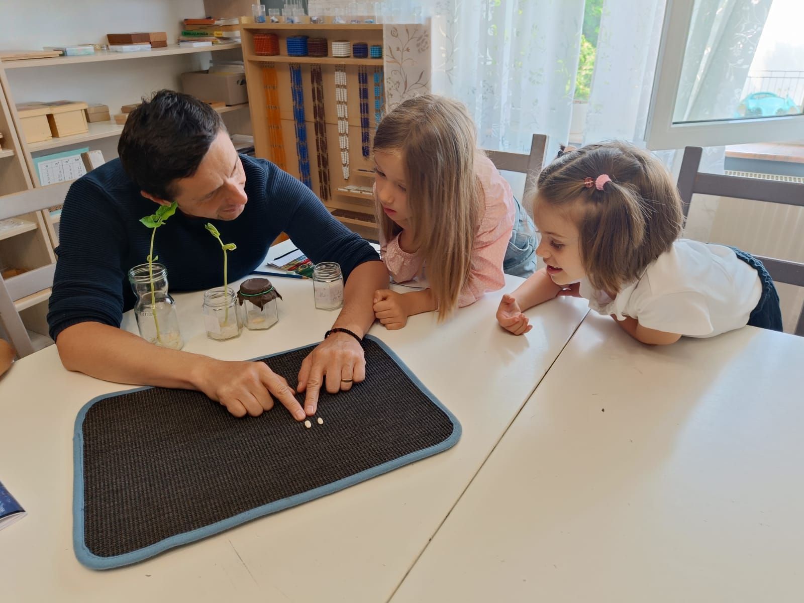 A man and two little girls are sitting at a table looking at a plant.