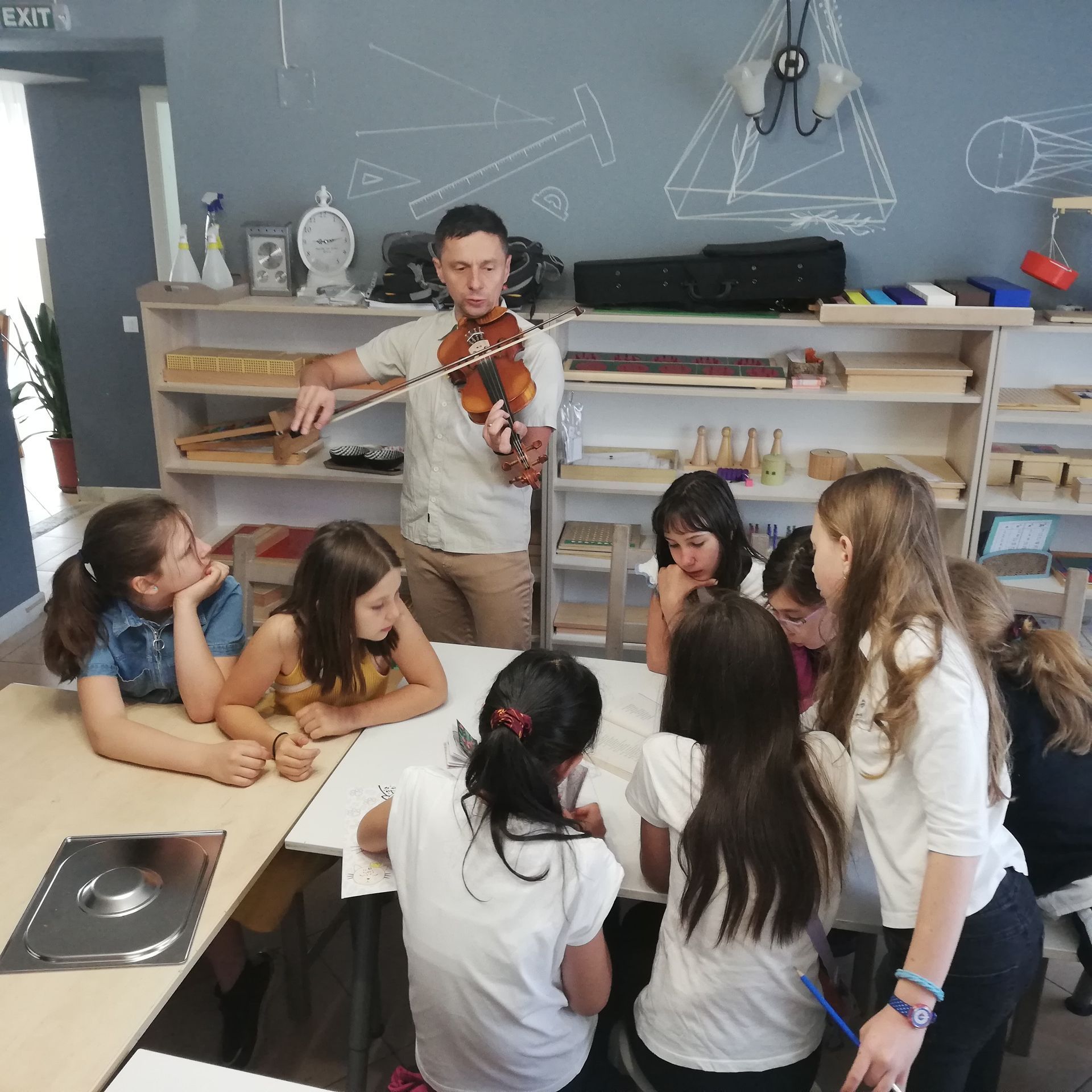 A man is playing a violin in front of a group of children