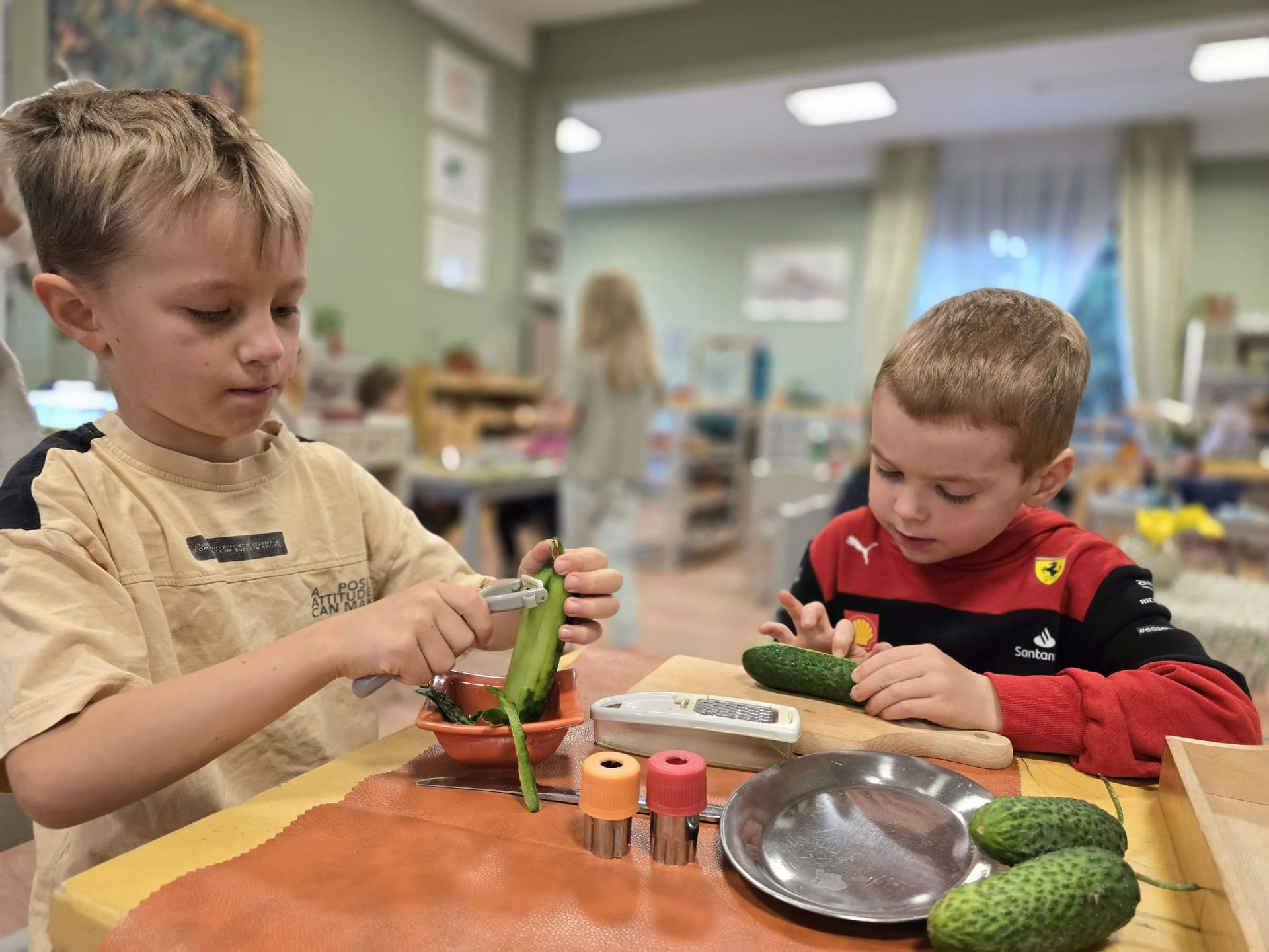 Two young boys are sitting at a table cutting cucumbers.