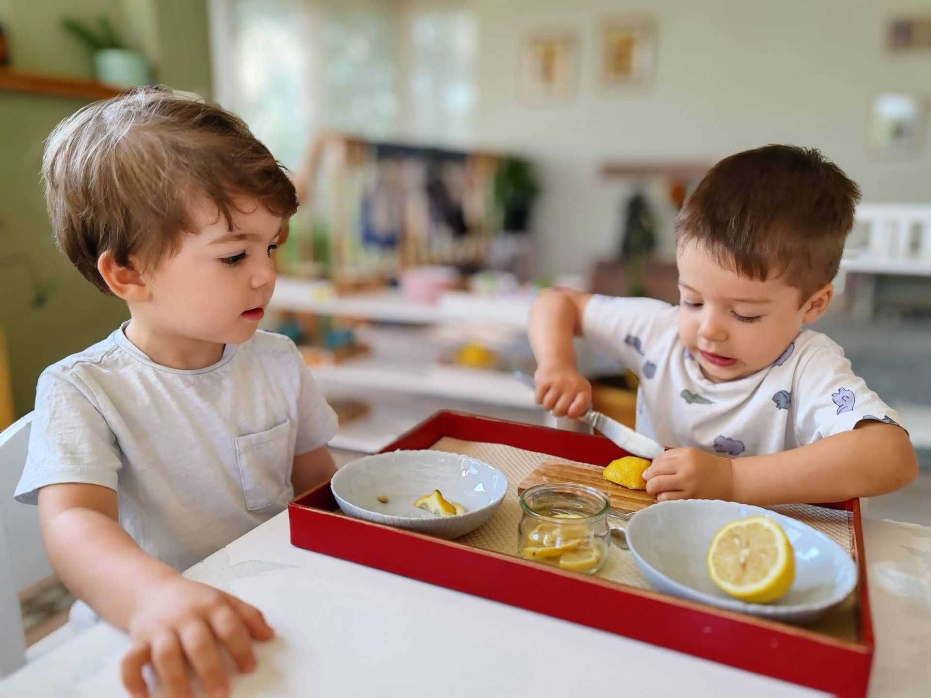 Two young boys are sitting at a table playing with lemons.