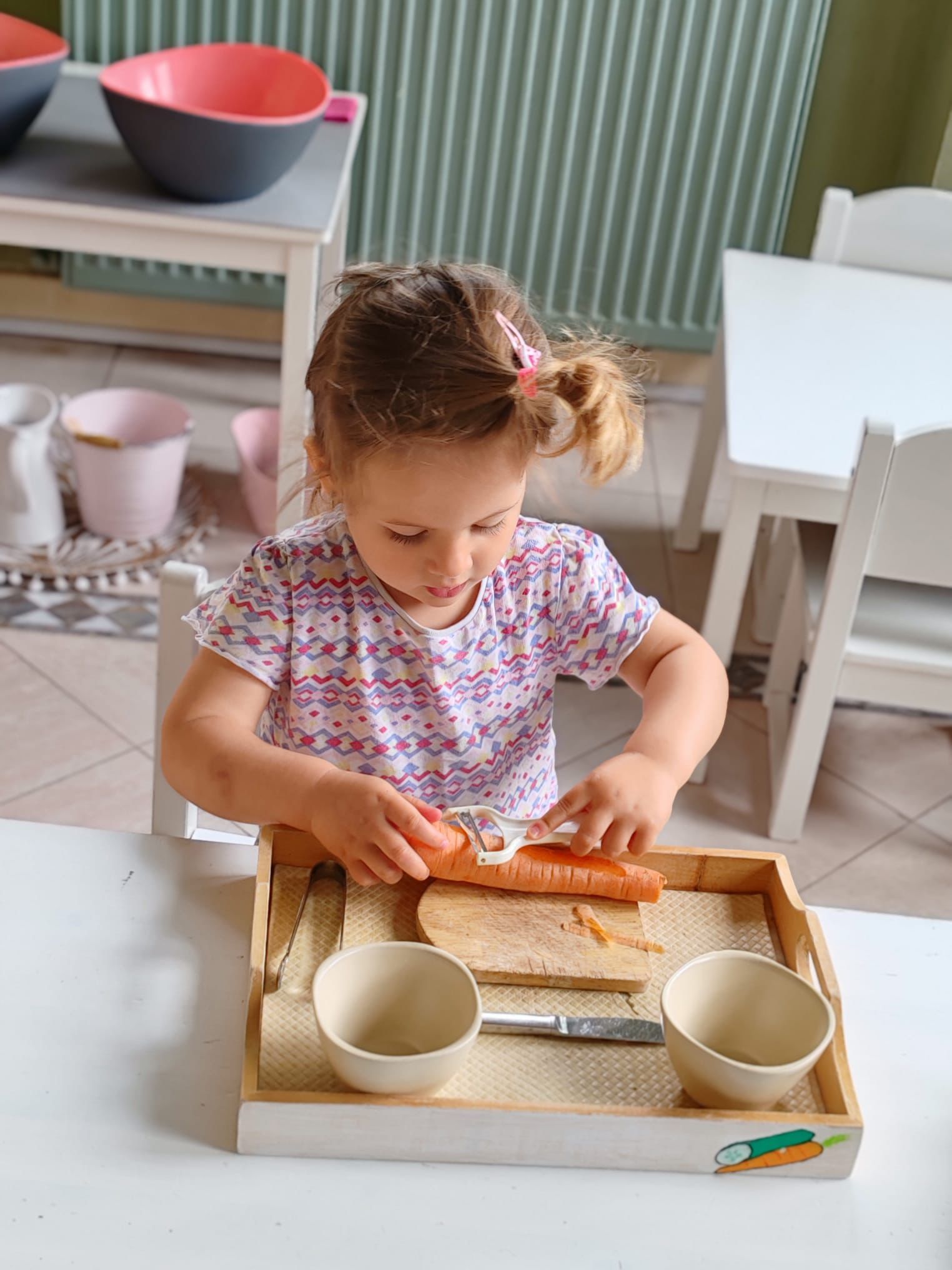 A little girl is cutting a carrot on a cutting board.