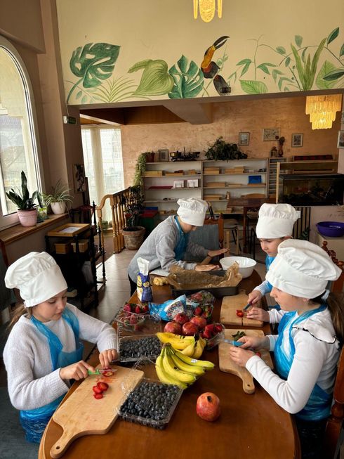 A group of children are sitting at a table cutting fruit.