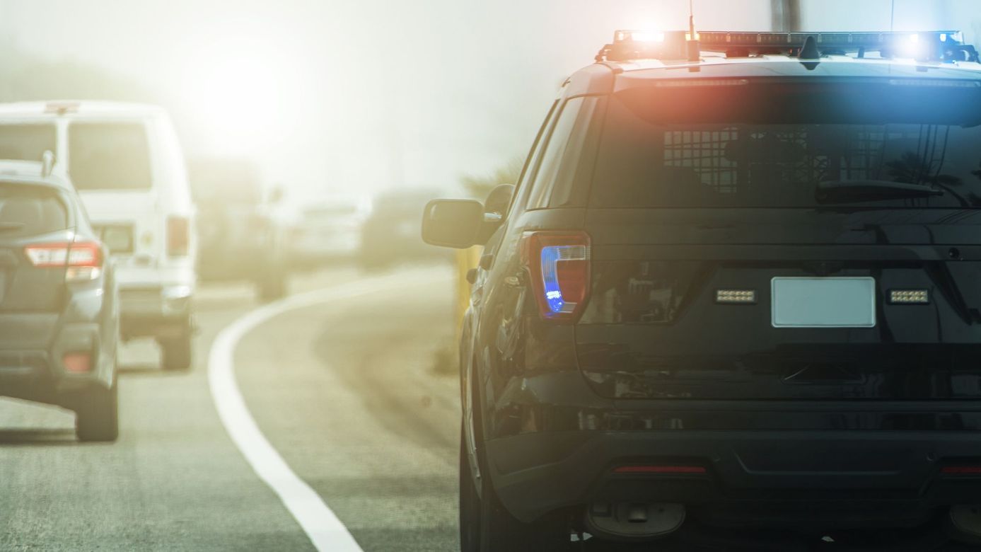 Police SUV with flashing lights on a foggy highway beside other vehicles