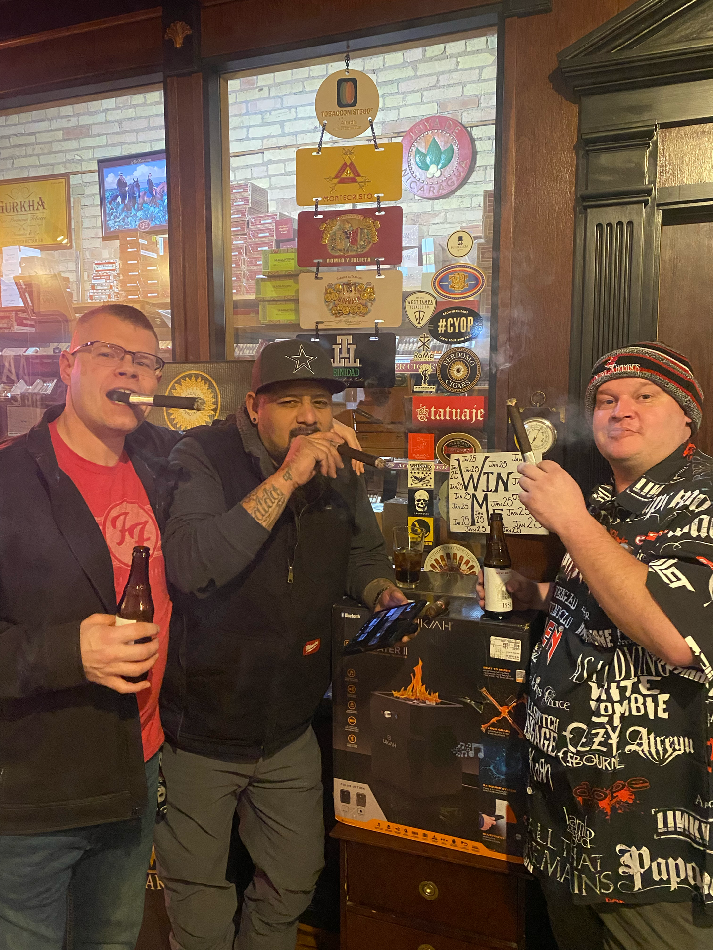 Three men smoking cigars posing in front of a walk in humidor
